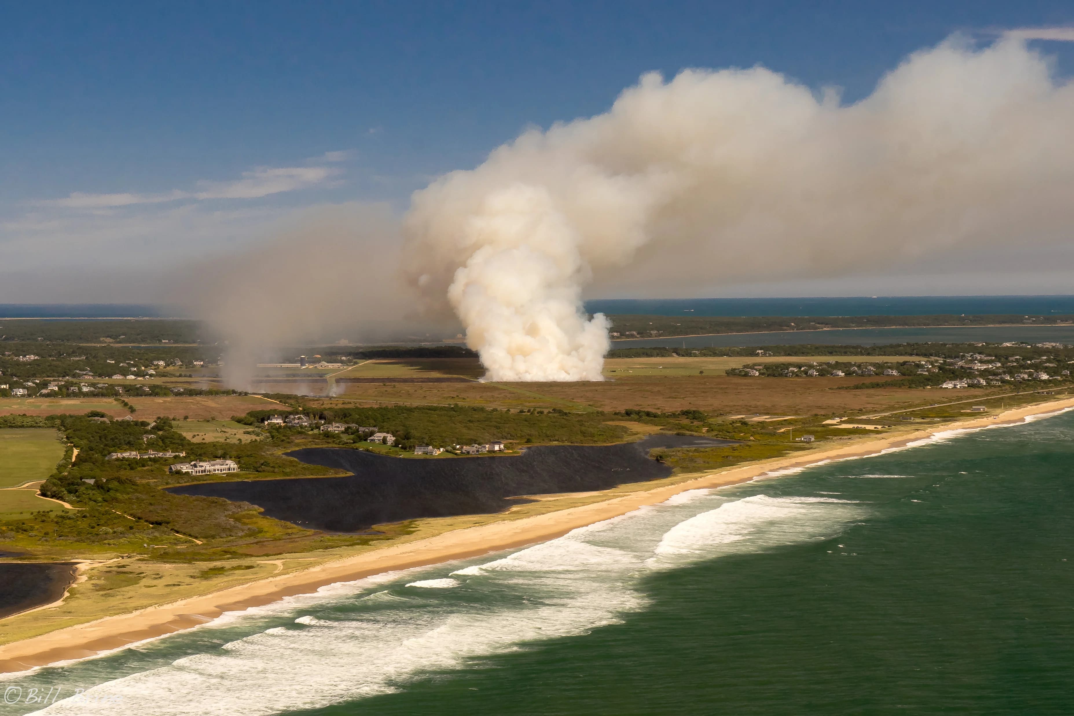 Aerial view of smoke rising from a prescribed burn at Katama beside the ocean.